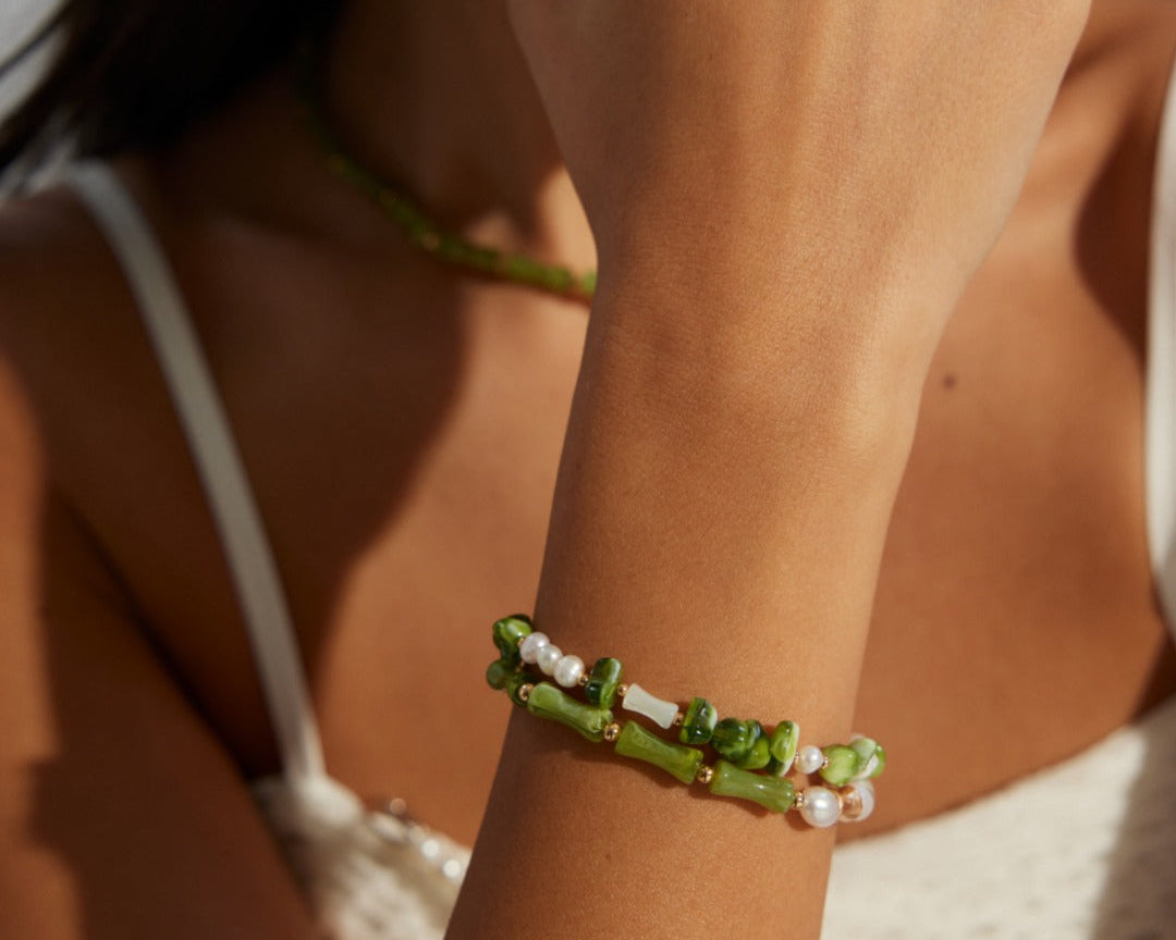 Close-up of a woman's arm wearing a green beaded bracelet against a neutral background